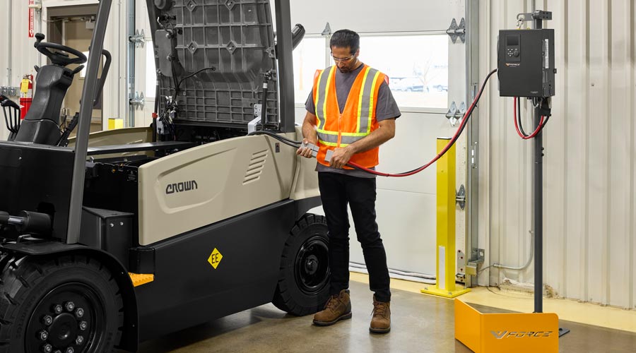 Crown forklifts lined up against the wall charging batteries in a indoor warehouse.