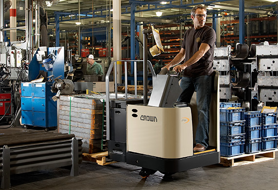 Operator moves a heavy load in a manufacturing setting using Crown PR series stand-up rider pallet truck